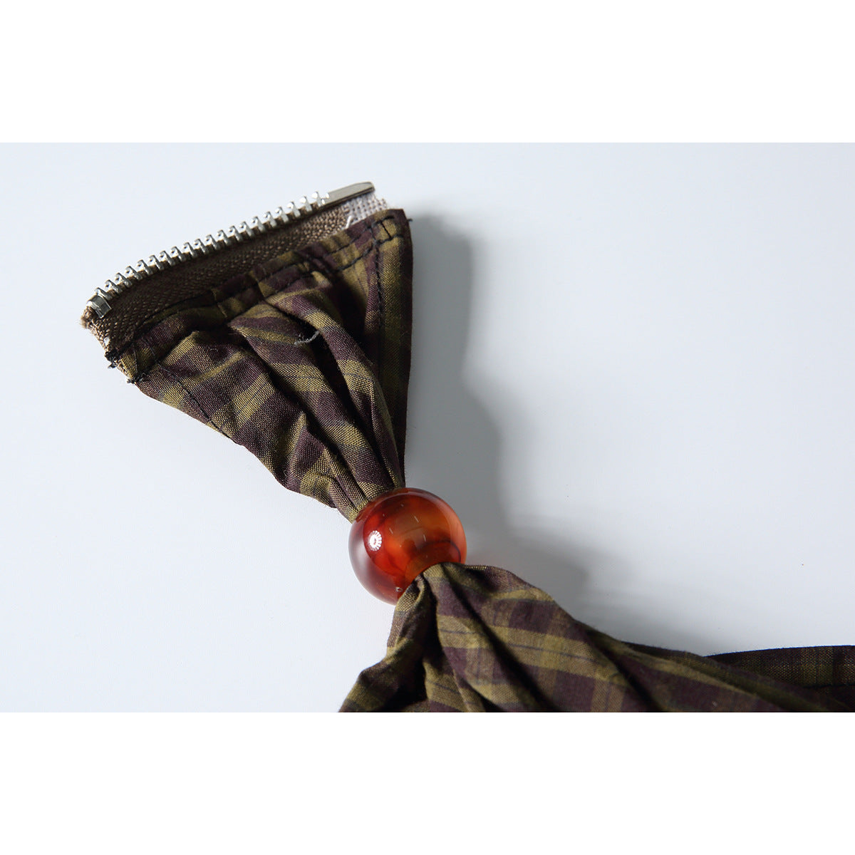 Close-up of a plaid fabric accent gathered with an amber bead and attached by a small zipper.