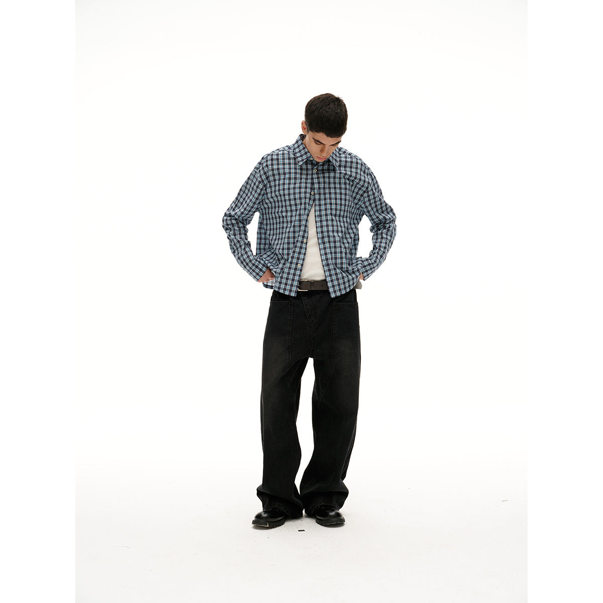 Model wearing a blue, gray, and black plaid button-up shirt over a white tank with wide black trousers.