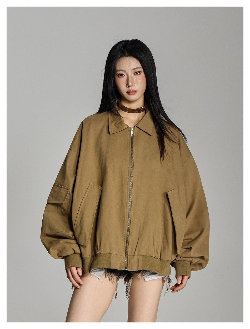 Model wearing a zipped tan-brown oversized jacket with a pointed collar, large front pockets, and sleeve flap pocket.