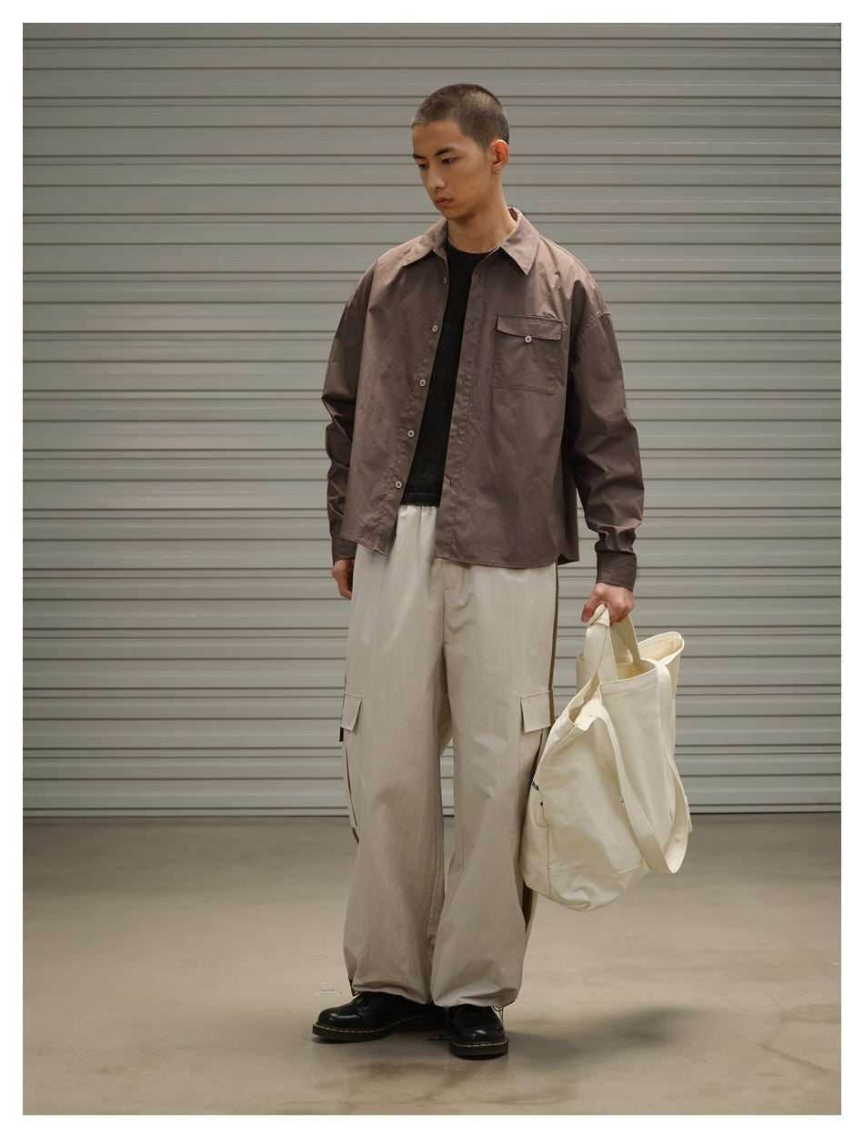 Model wearing light khaki wide-leg cargo pants with a brown shirt and black boots, holding a cream tote bag