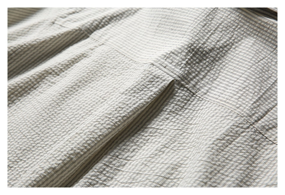 Close-up of cream fabric with fine dark stripes and a stitched seam.