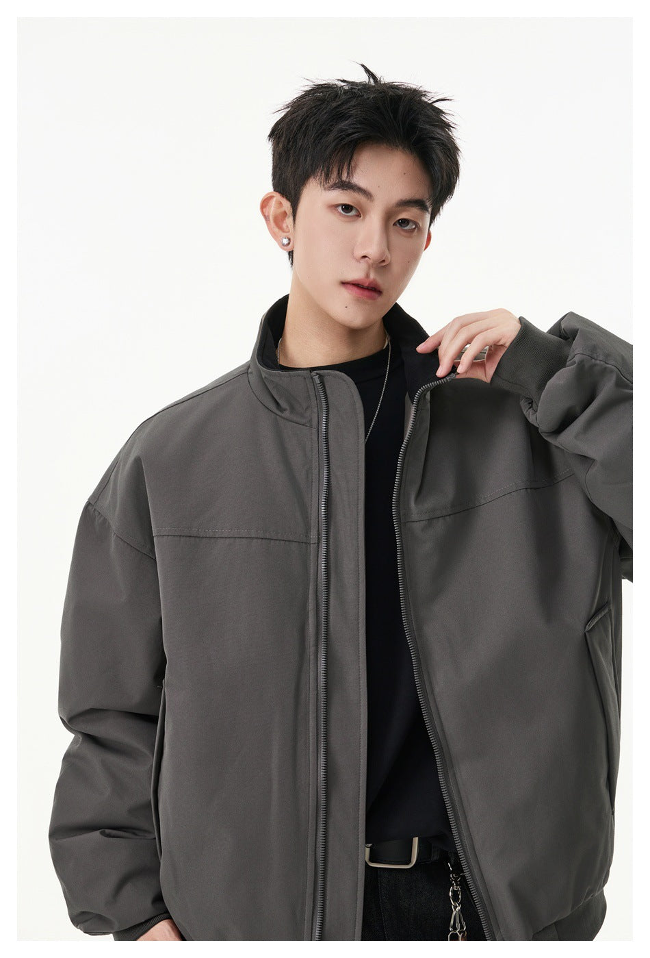 Upper-body view of a model wearing an open charcoal-gray zip jacket over a black top.