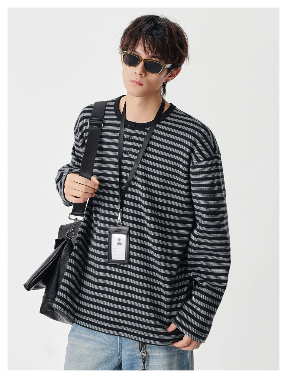 Model wearing a loose black and gray striped long-sleeve henley with a short button placket.