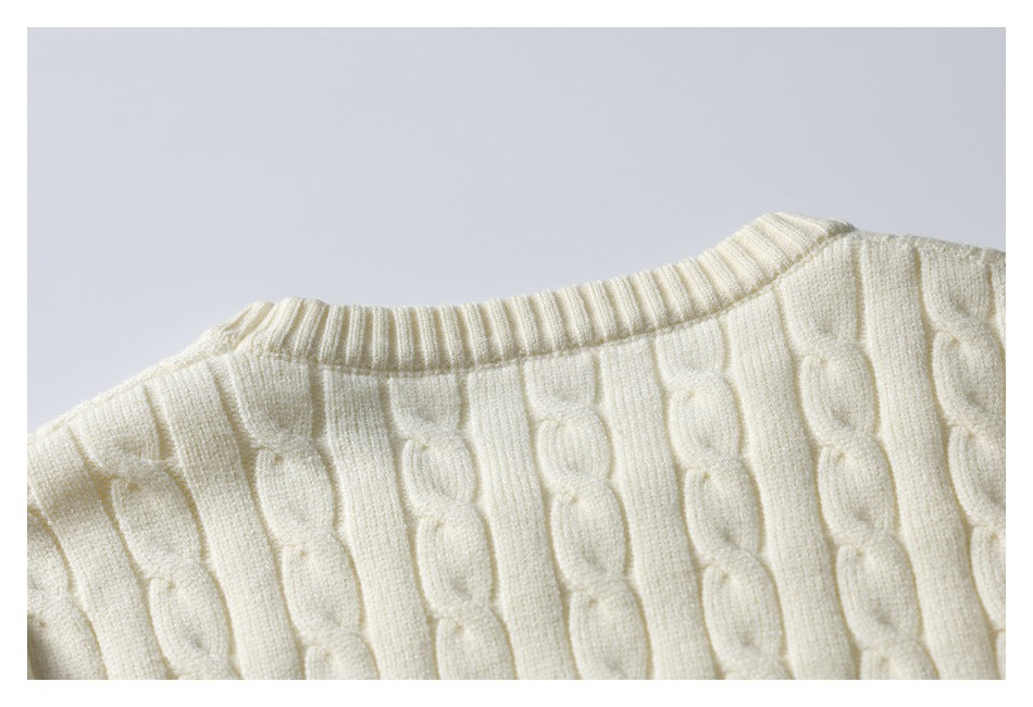 Close-up of an ivory cable-knit sweater showing the ribbed neckline and raised vertical knit pattern.