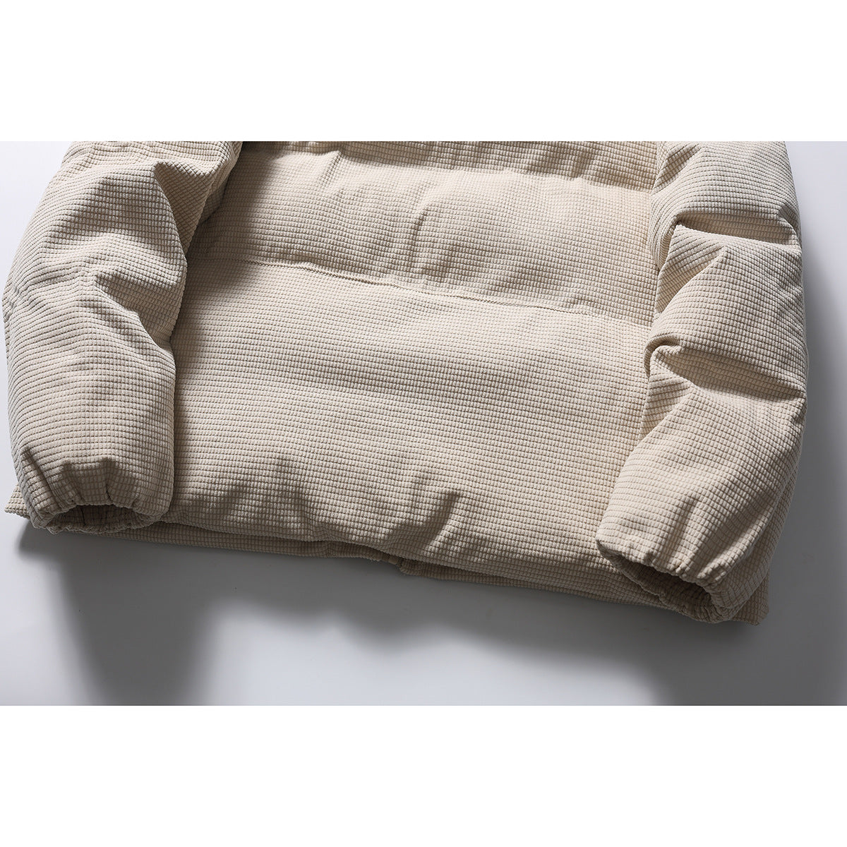 Cream textured padded jacket laid flat, showing its back panel and gathered sleeves; the upper edge is cropped.