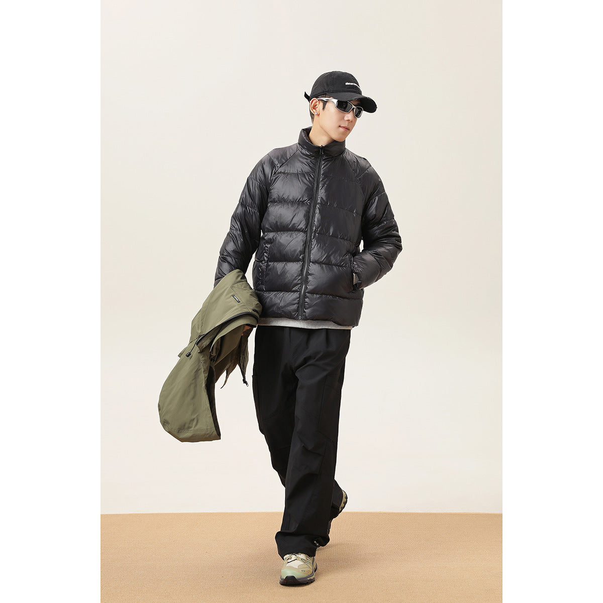 Model wears a black quilted jacket and carries an olive hooded jacket over one arm.
