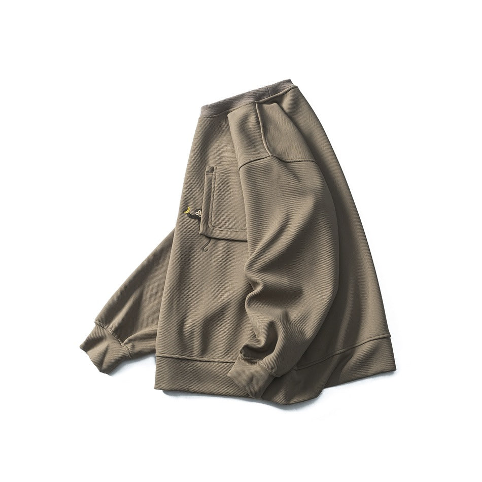 Three-quarter view of a taupe crewneck sweatshirt laid flat, showing the chest pocket, small motif, and ribbed trim.