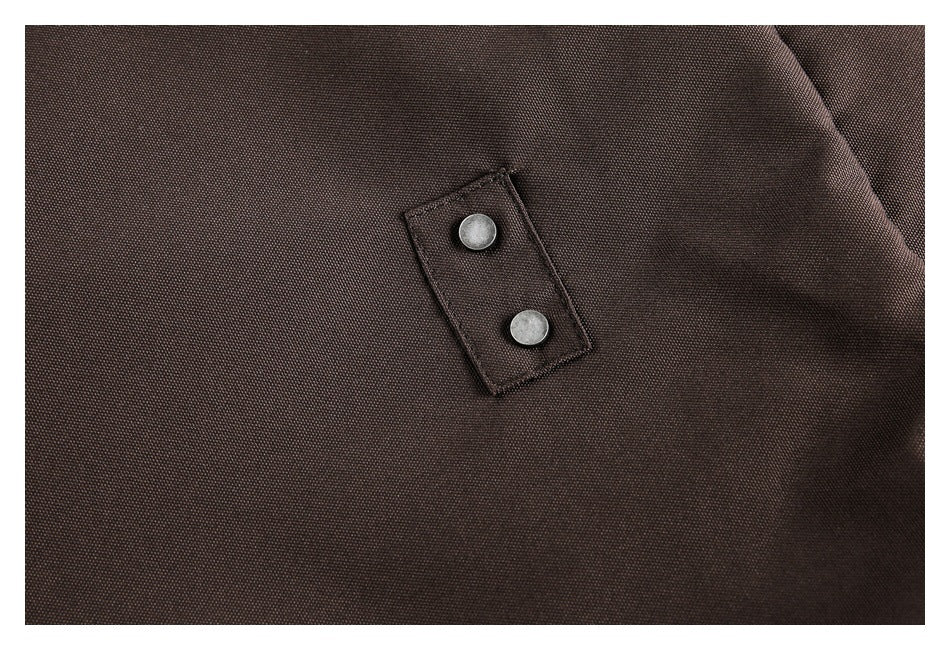 Close-up of two round metal snaps on a small tab over dark brown garment fabric.