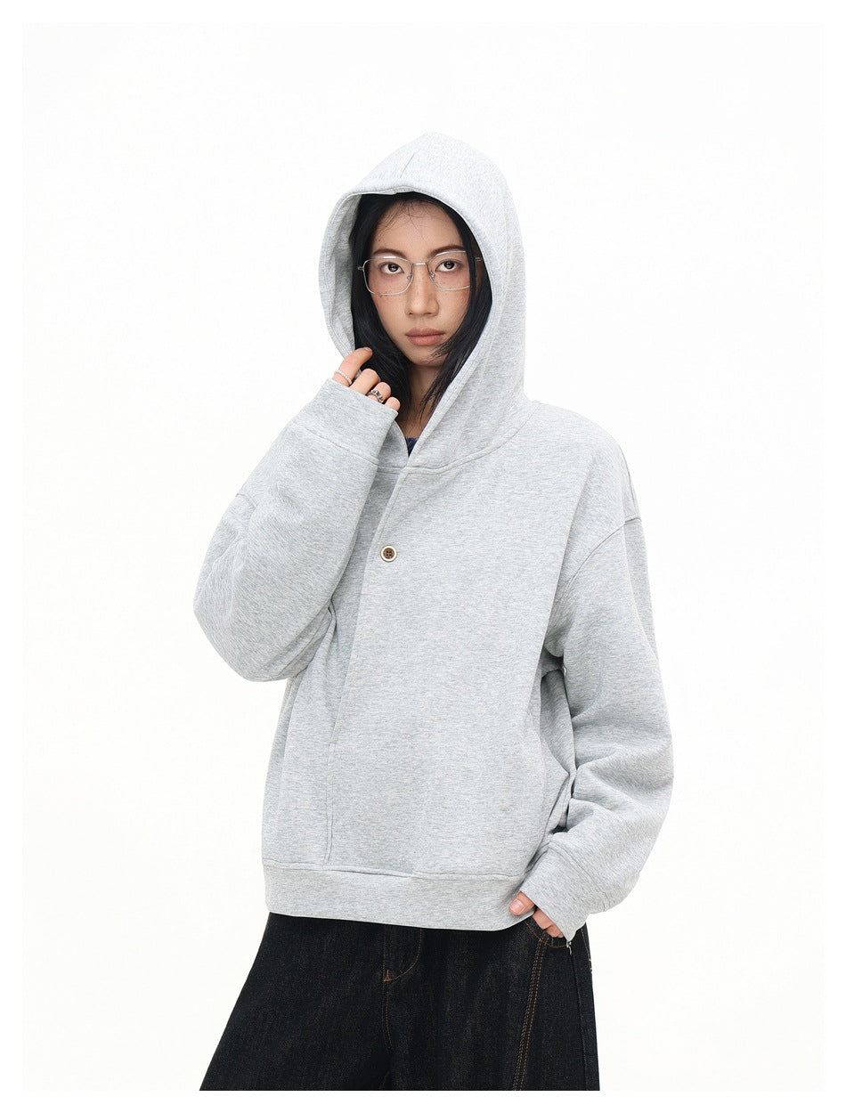 Close view of the light gray sweatshirt's hood, buttoned front, roomy sleeves, and ribbed hem on a model.