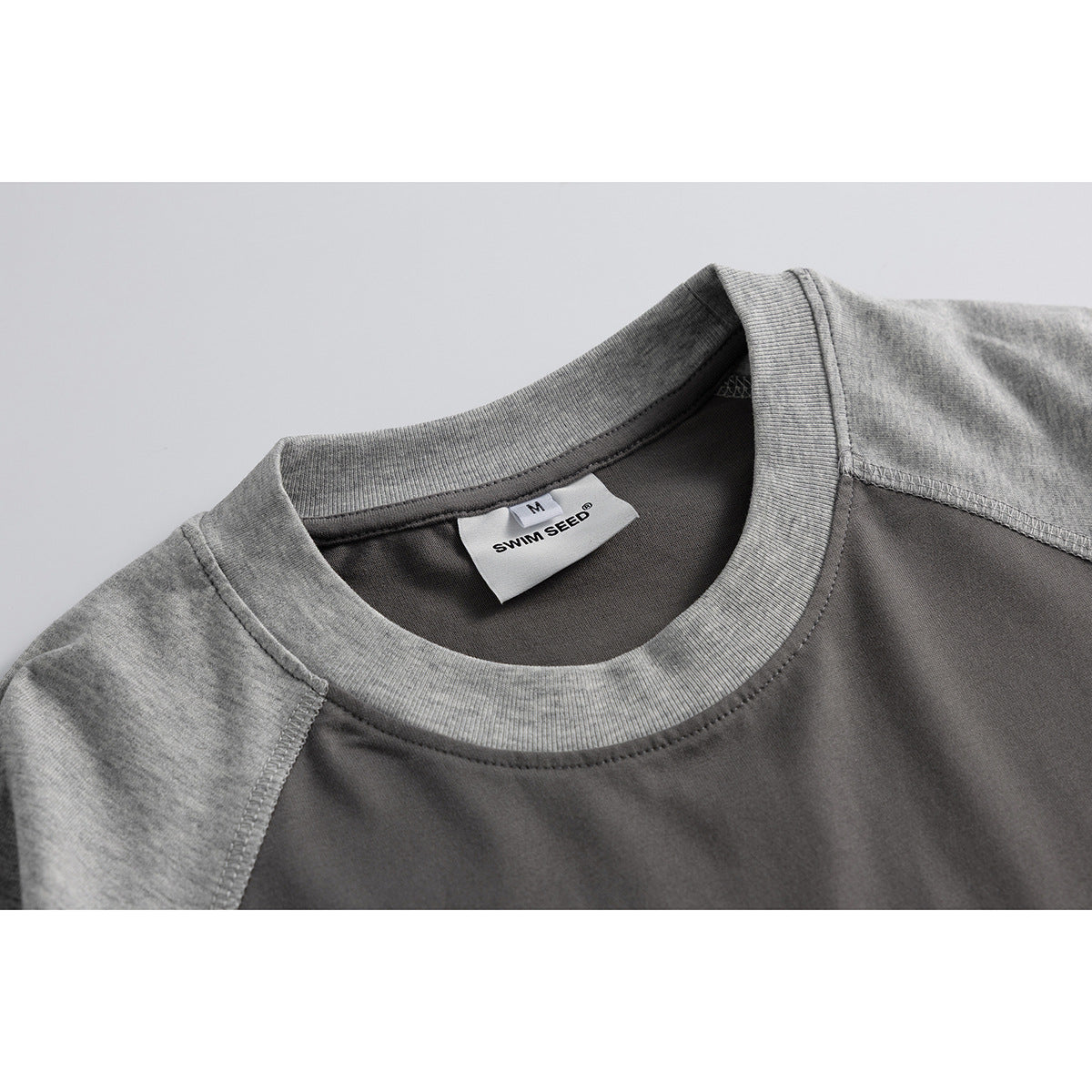 Close-up of a charcoal raglan T-shirt neckline with heather-gray collar and sleeves; the sewn label shows size M.