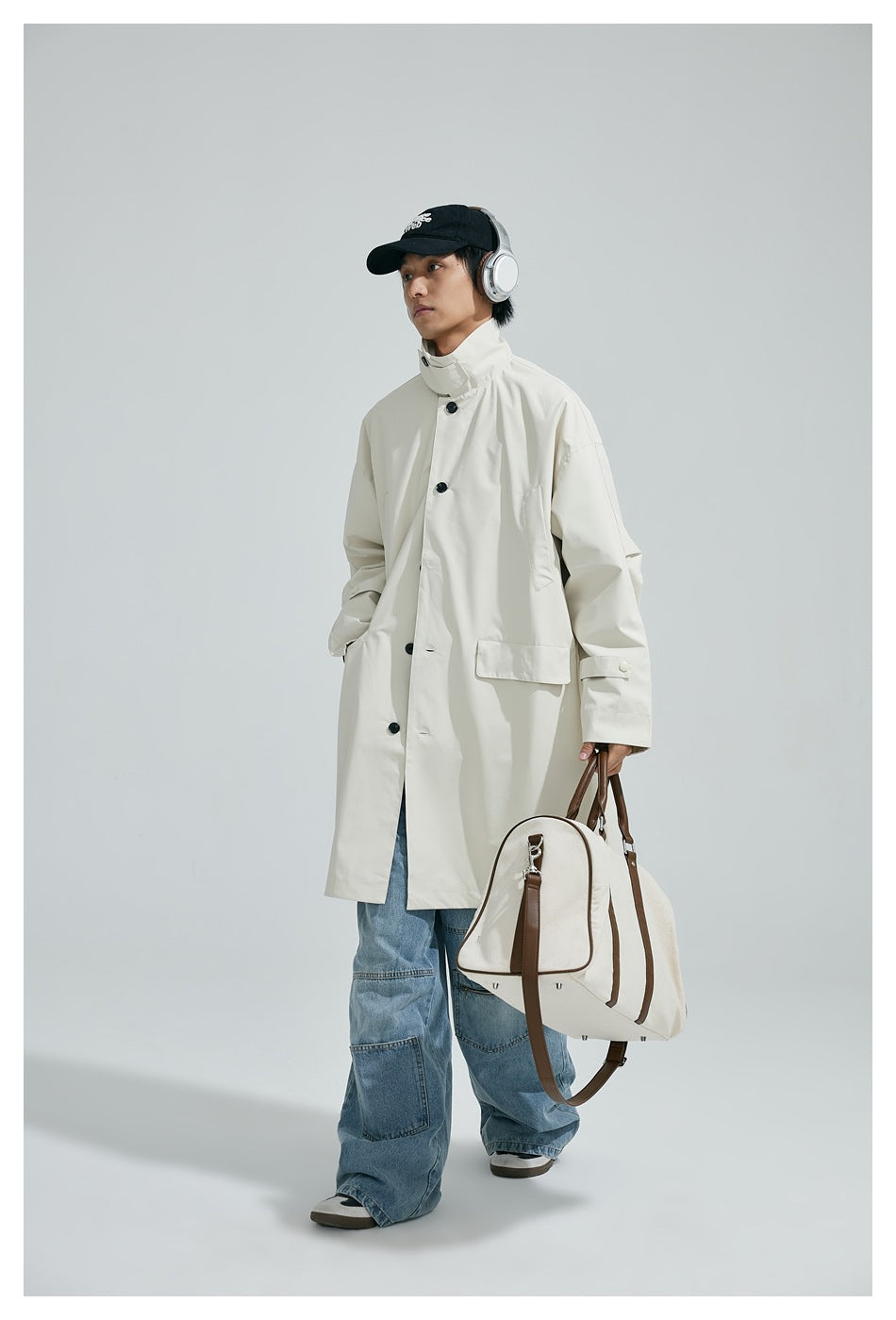 Person wearing an ivory long coat with a high collar and flap pockets, paired with loose blue jeans.