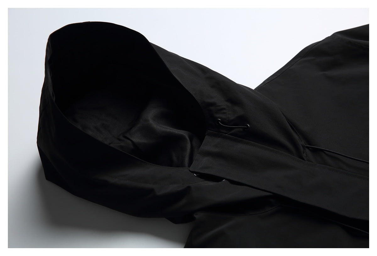 Close-up of a black hood and its drawcord eyelet against a light background.