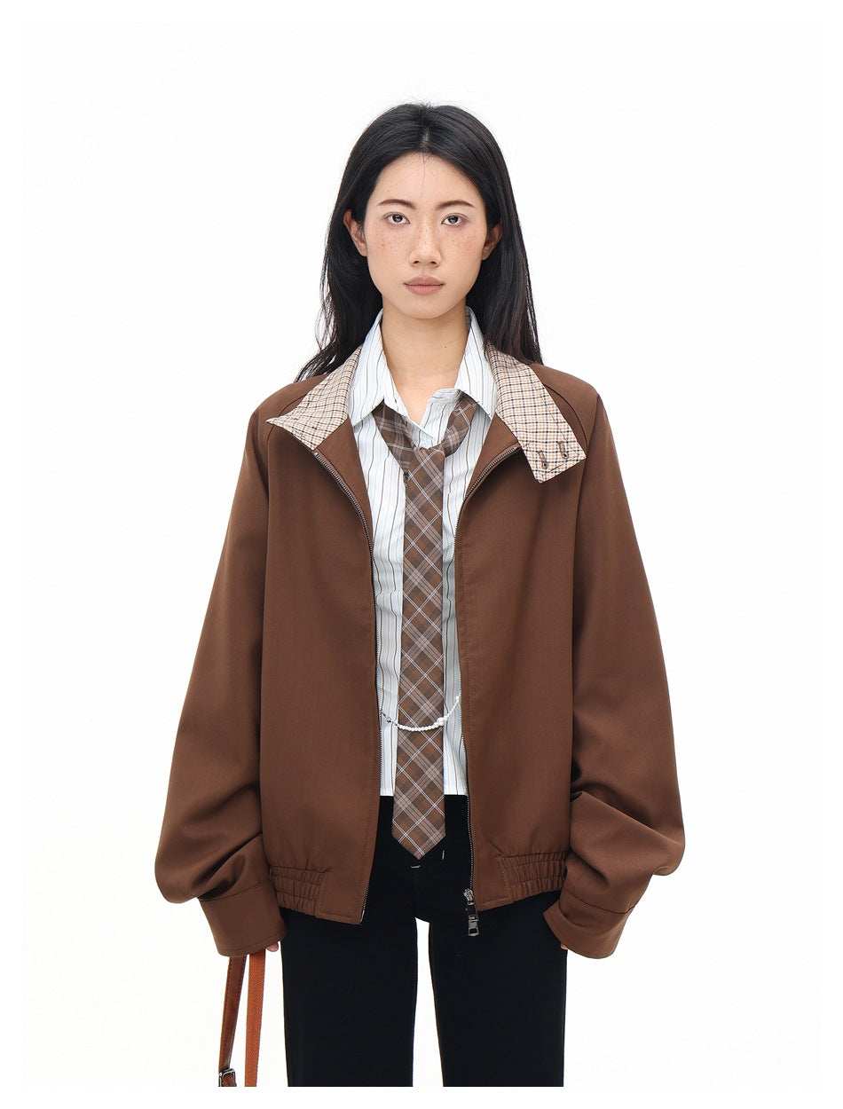 Model wearing open brown zip jacket with plaid undercollar over striped shirt, plaid tie and black pants