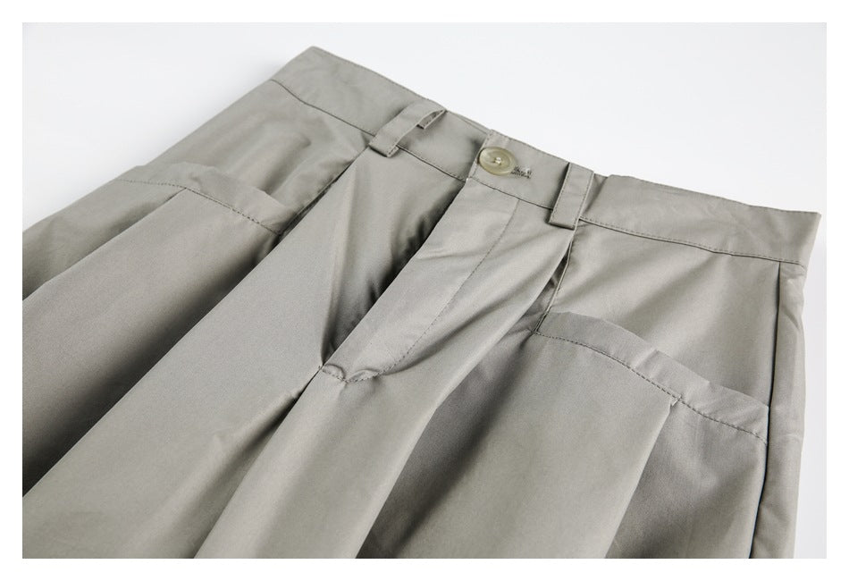 Close-up of taupe-gray trousers showing the front waistband, button, belt loops and pleated pockets.