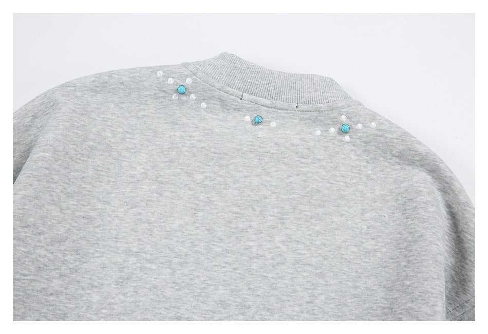 Close-up of a heather gray garment shoulder with a ribbed collar, turquoise buttons, and small white accents.
