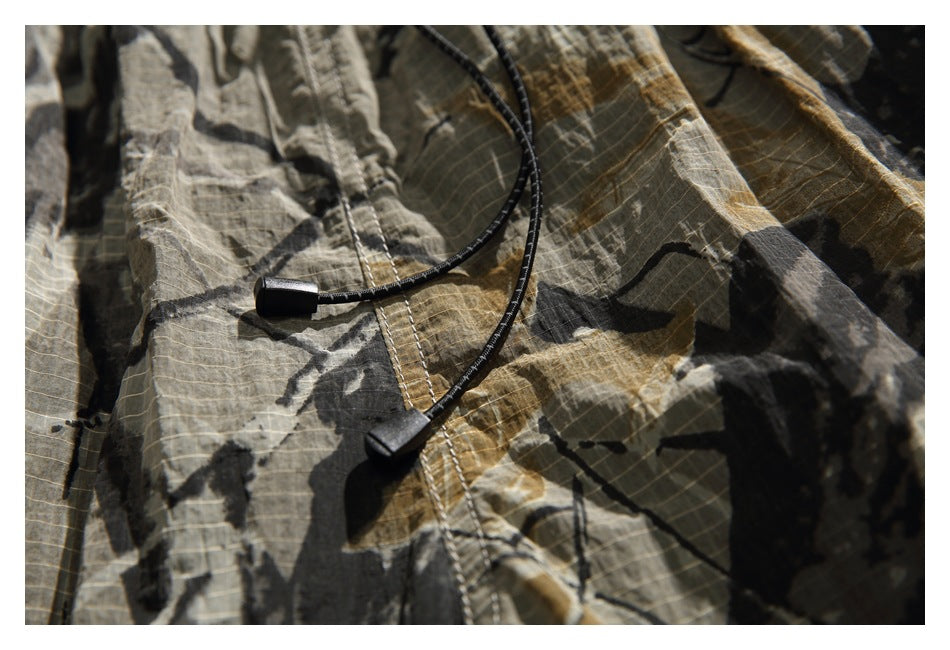 Close-up of camouflage shorts with black elastic drawcords and a stitched grid pattern.