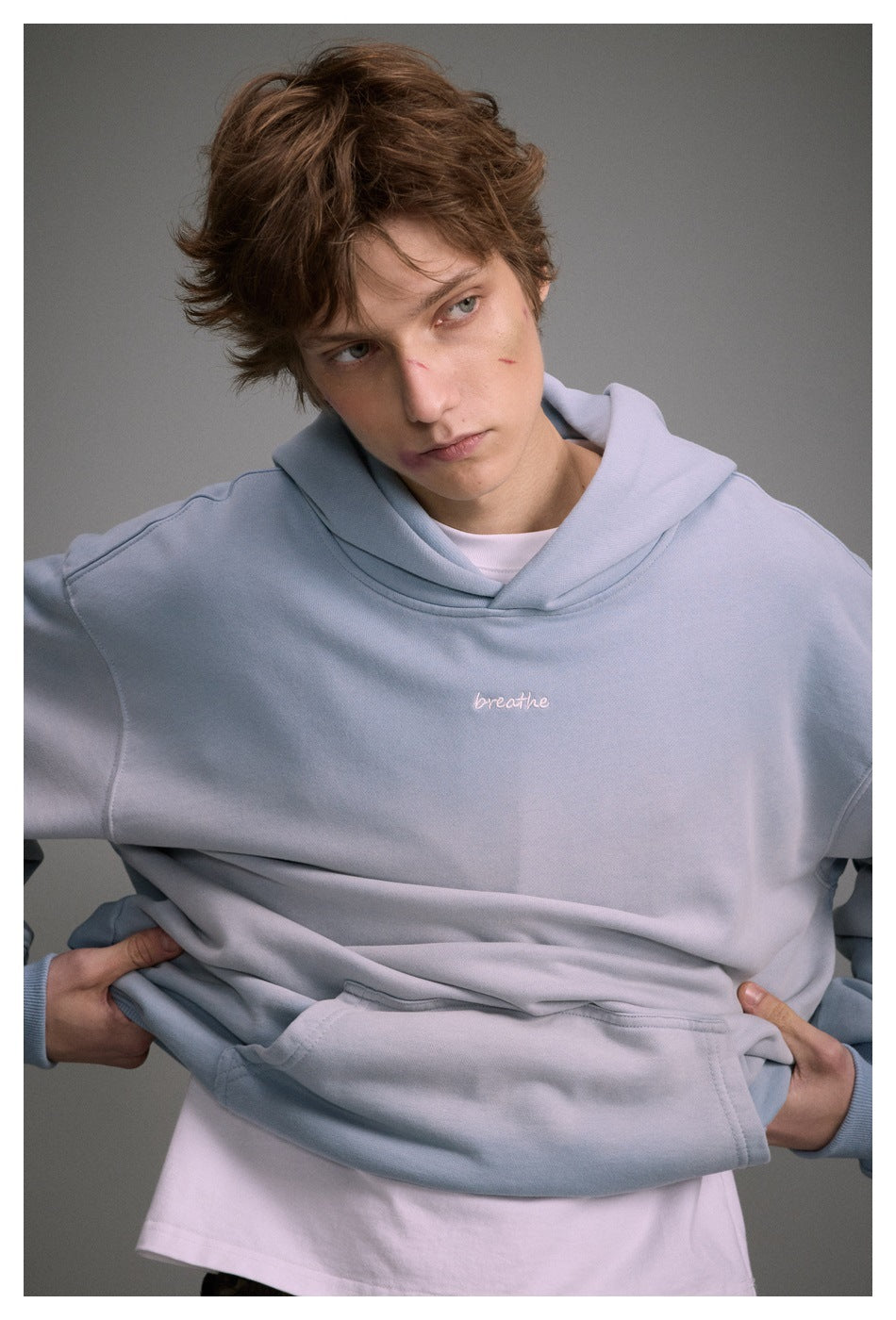 Close view of a model wearing a pale blue hoodie with a white “breathe” chest embroidery and kangaroo pocket.