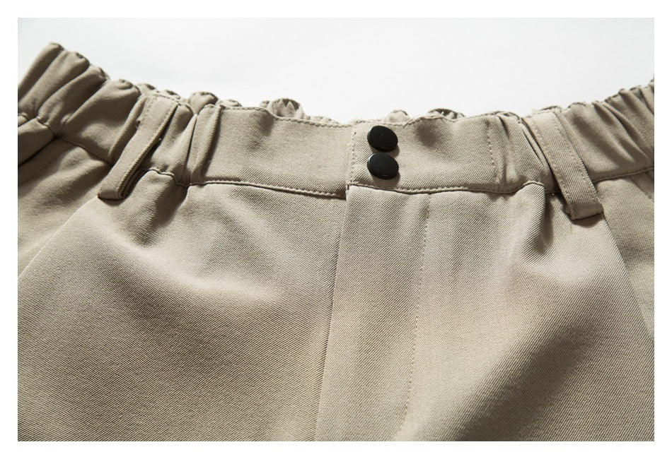 Close-up of beige shorts showing an elasticated waistband, belt loops, and two black buttons.