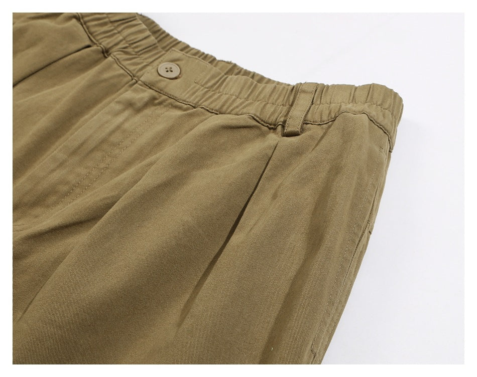 Angled close-up of khaki pants showing the elastic waistband, button, belt loop, pleat, and pocket opening.