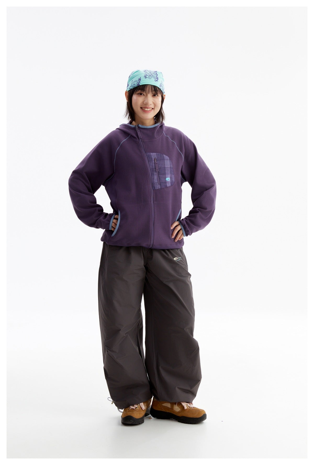 Woman models a purple hooded zip jacket with blue piping and a checked chest pocket, paired with dark pants.