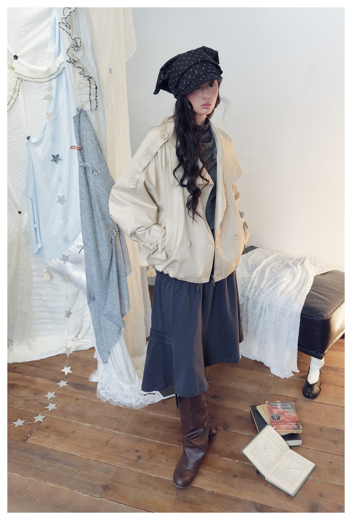 Model wearing a cream oversized jacket with a gray top and navy wide-leg bottoms, styled with a black polka-dot headscarf.