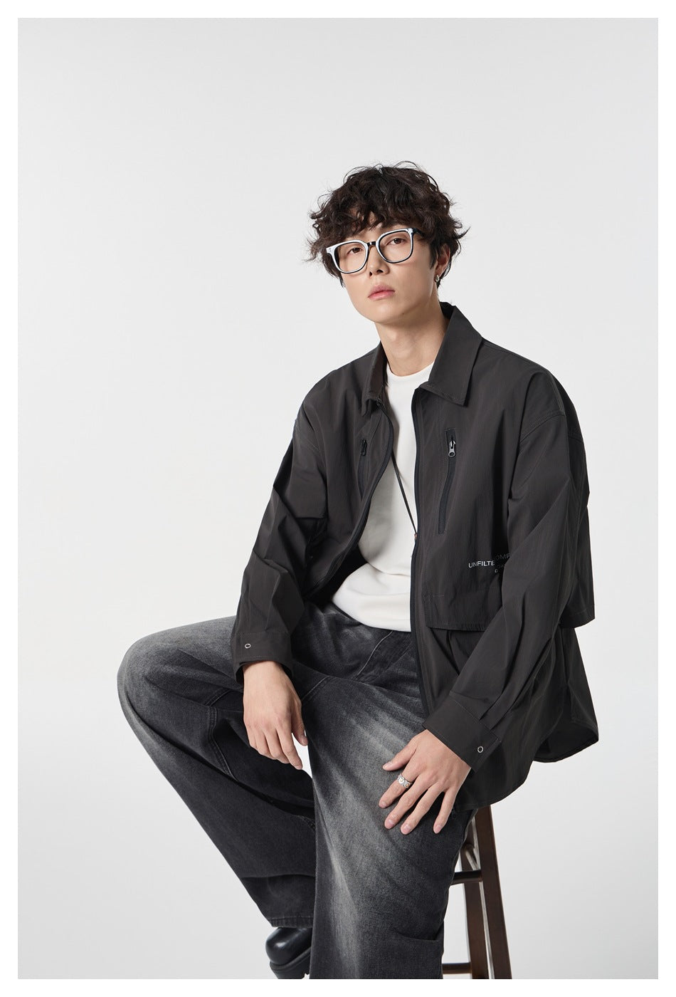 Seated model wearing a black utility jacket with zip chest pockets over a white shirt.