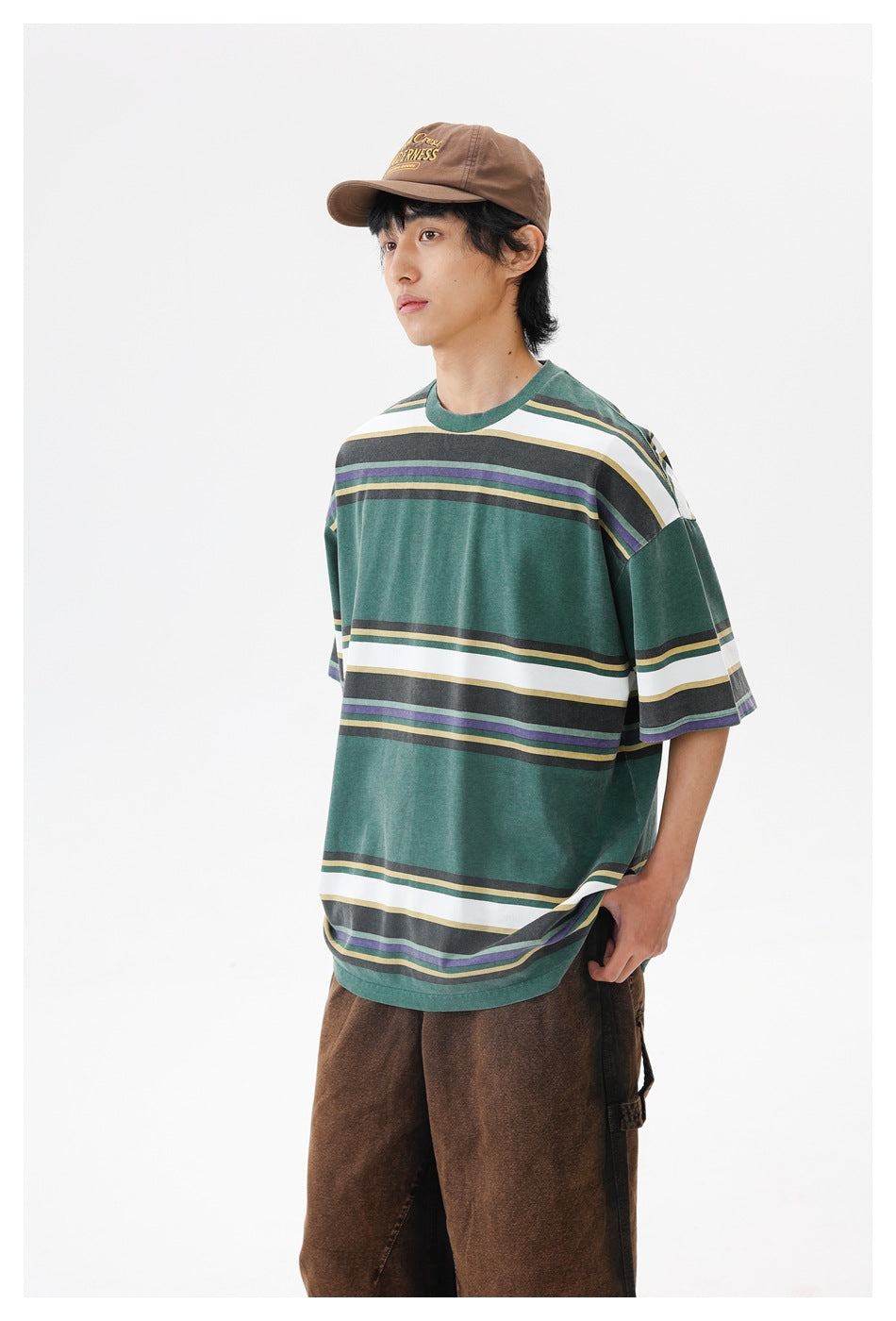 Closer view of a model wearing a forest-green oversized T-shirt with broad white and narrow multicolor horizontal stripes.