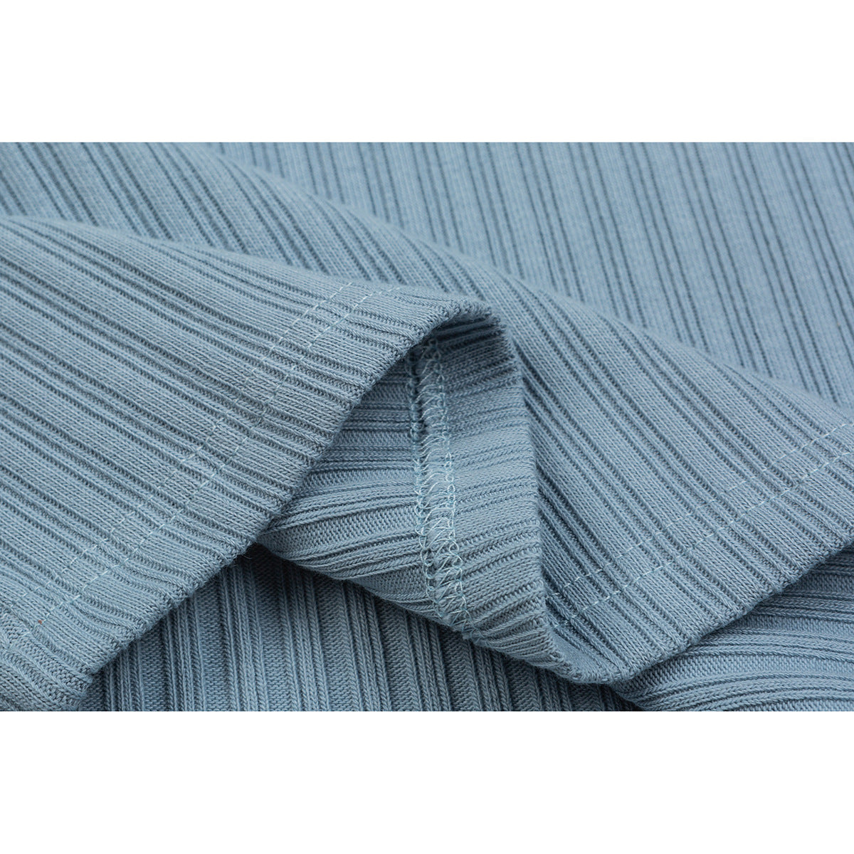 Close-up of light blue ribbed fabric folded to show the stitching along a garment seam.