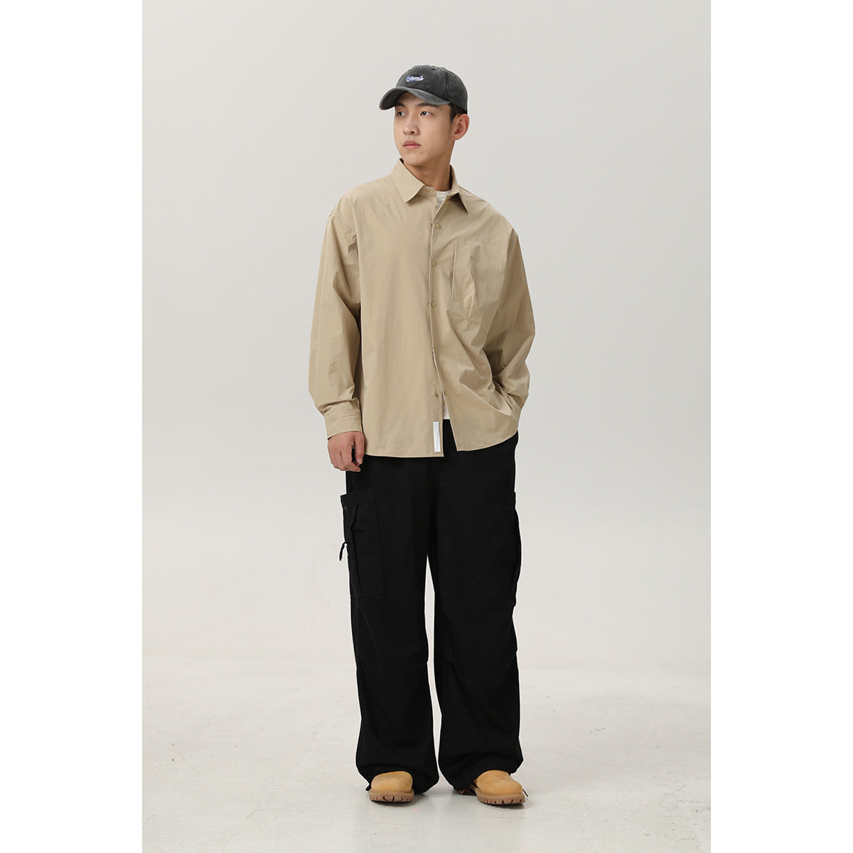Front view of a model in a beige button-front shirt with chest pocket and loose black cargo pants.