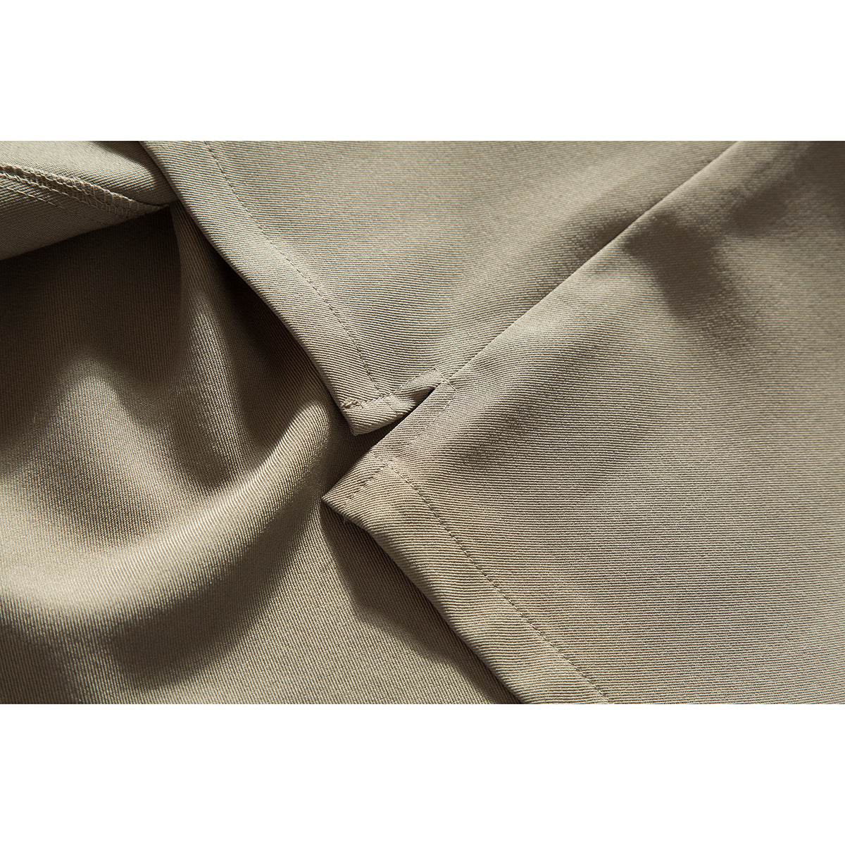 Close-up of intersecting stitched seams on taupe shirt fabric.
