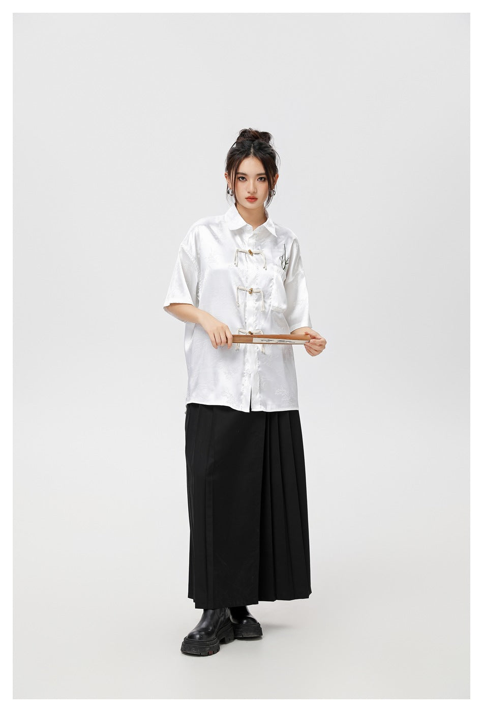 Model wearing a white patterned short-sleeve shirt with frog closures and a long black skirt.