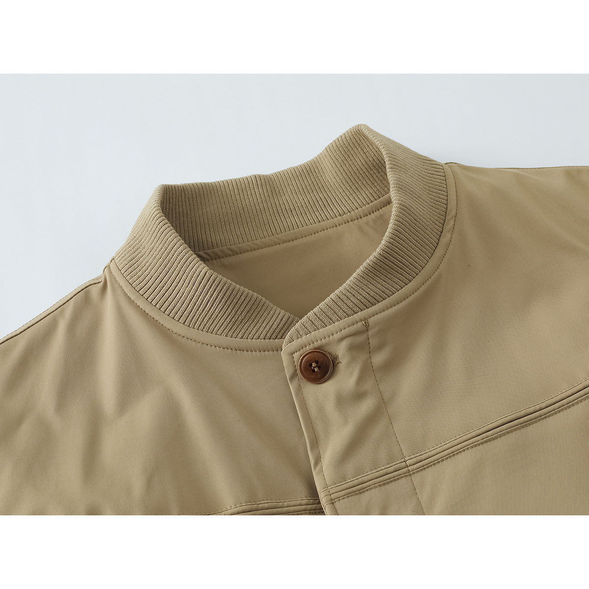 Close-up of a tan jacket’s ribbed stand collar, button-front placket, and stitched chest seam.