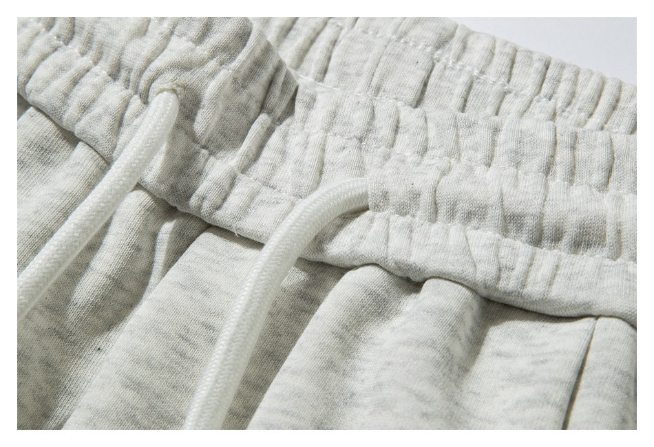 Close-up of the gathered elastic waistband and white drawstrings on light heather-gray sweatpants.