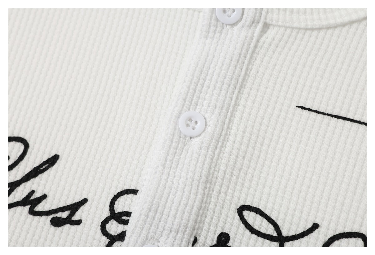 Close-up of a white ribbed button-front garment with partial black script print.
