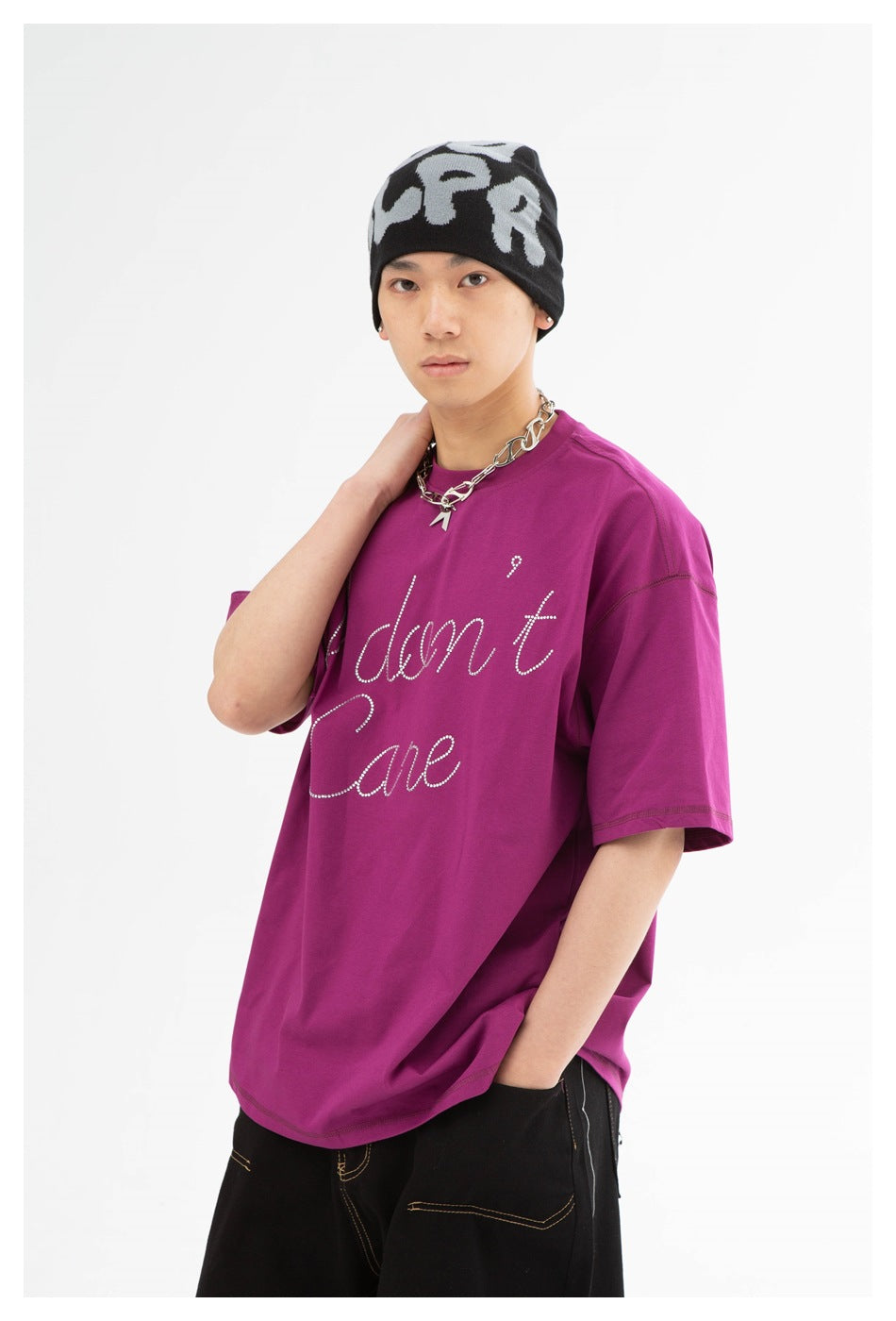 Model wearing an oversized magenta T-shirt with rhinestone script, a black-and-gray beanie, and black pants.