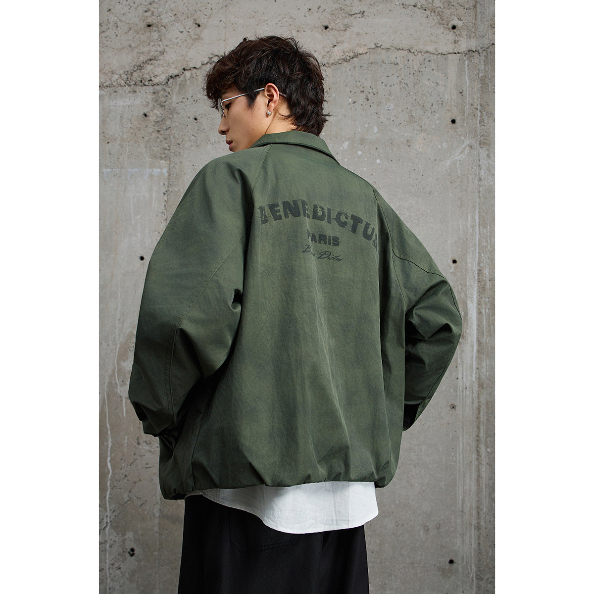 Rear view of a person wearing an oversized olive-green jacket with large dark lettering across the back.