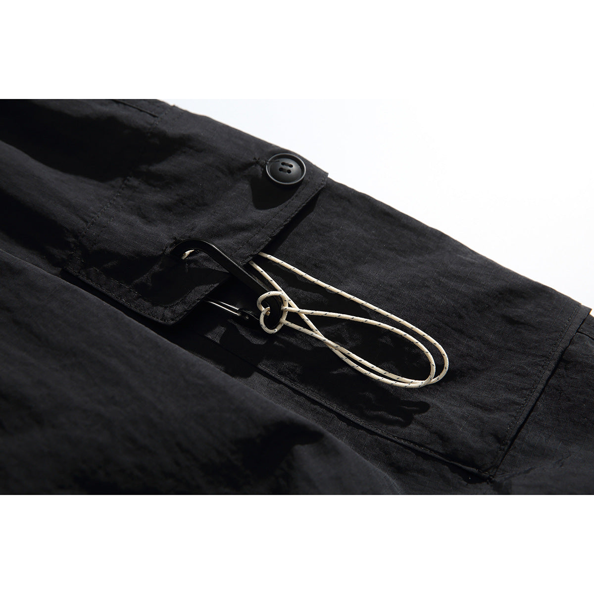 Close-up of black cargo trousers with a buttoned pocket flap and light-colored looped drawcord.