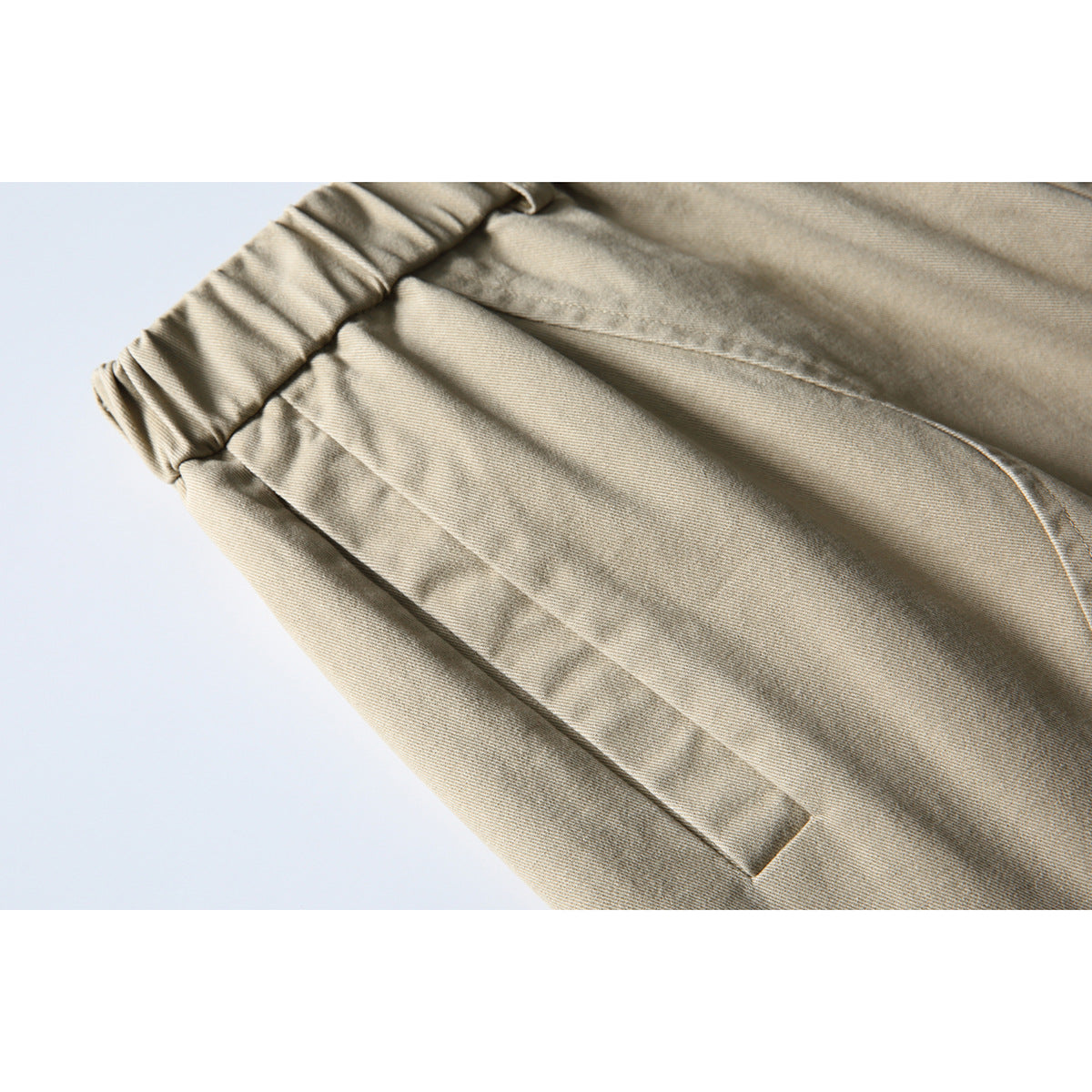 Close-up of beige trousers showing the gathered waistband and a slanted front pocket.