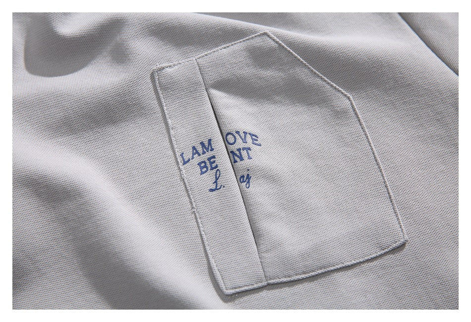 Close-up of a light gray shirt pocket with partially obscured blue lettering.