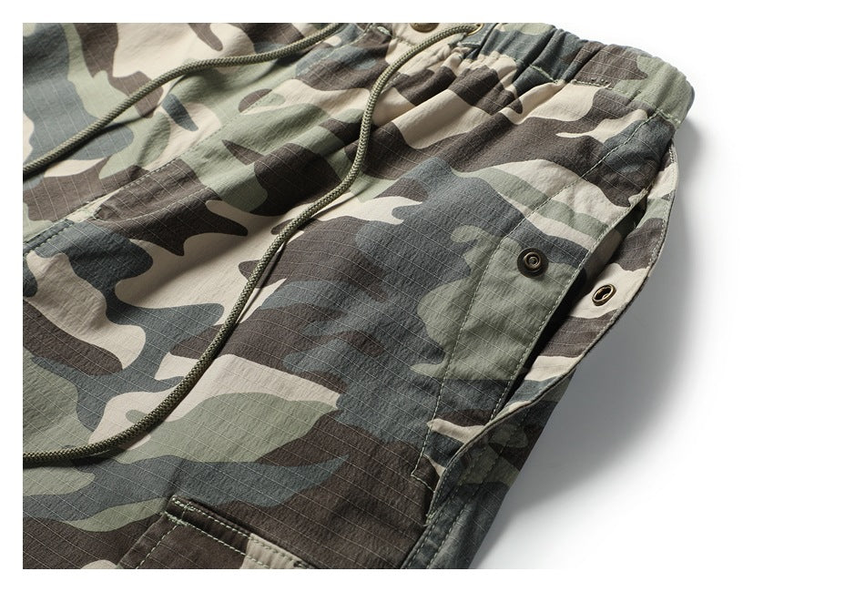 Close-up of camouflage cargo trousers showing the elastic drawstring waist and a snap-button side pocket.