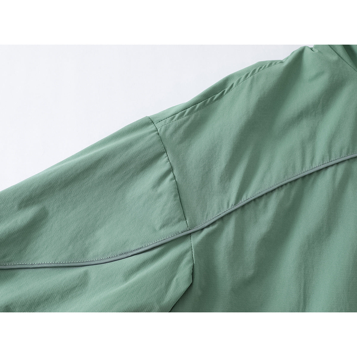 Close-up of a sage-green jacket’s sleeve and shoulder, showing curved piping and seam details.