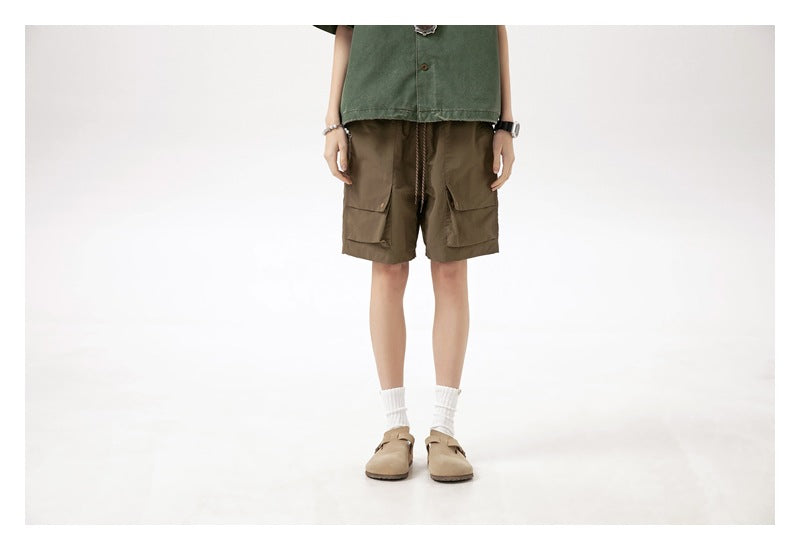 Cropped front view of a model wearing brown cargo shorts with a drawstring waist and flap pockets.