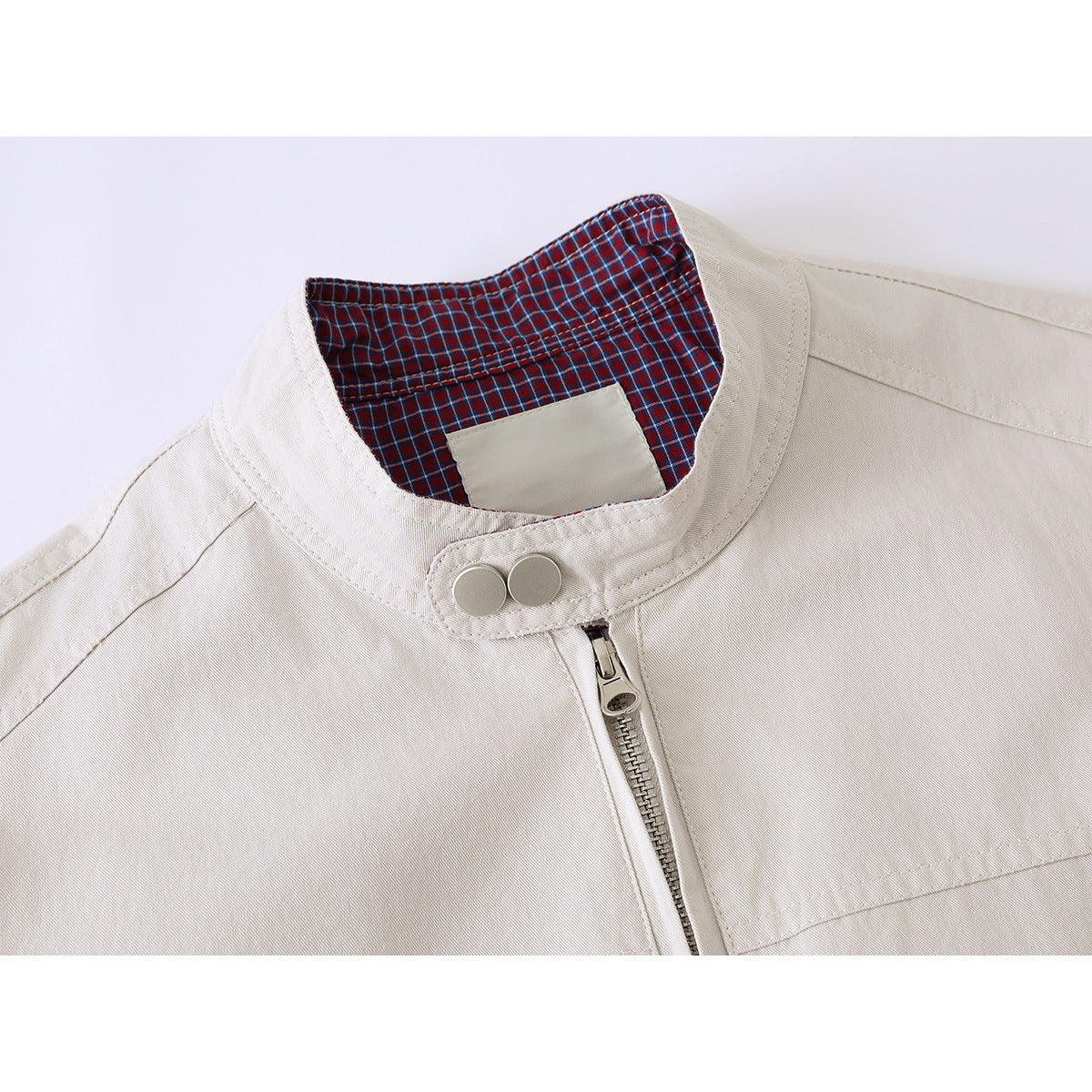 Close-up of an ivory jacket’s stand collar, red-and-blue plaid lining, snap buttons, and front zipper.