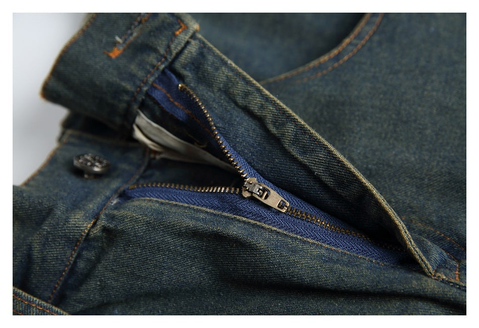 Close-up of dark blue jeans with the fly open, showing a metal zipper, button, and orange stitching.