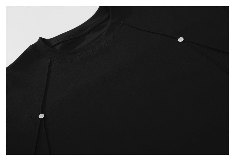 Close-up of a black garment’s crew neckline, panel seams, and small silver snap fasteners.