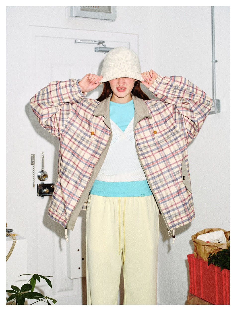 Model wearing open plaid jacket over a white knit top and aqua tee with pale yellow pants and cream bucket hat