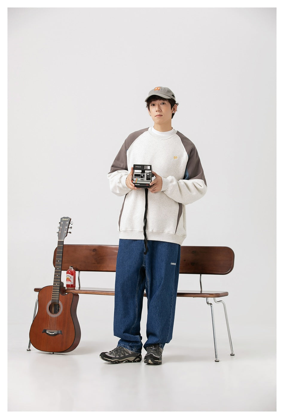 Model standing in an off-white sweatshirt with gray and blue color-block panels and loose blue jeans.