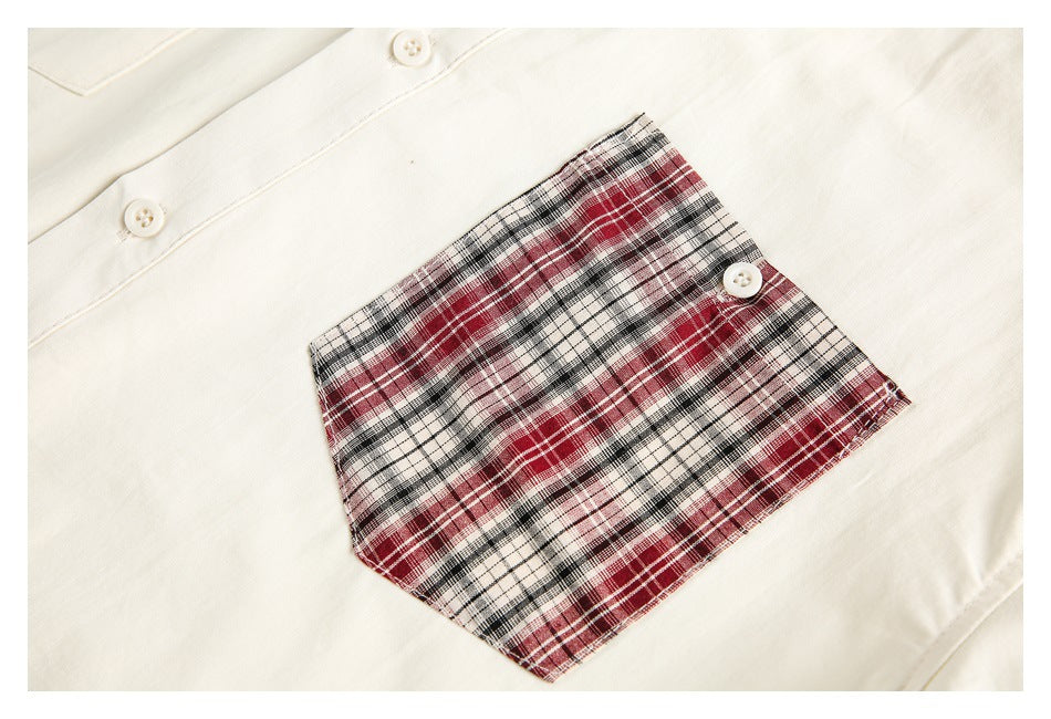 Close-up of a red, black and white plaid chest pocket with a white button on an ivory shirt.