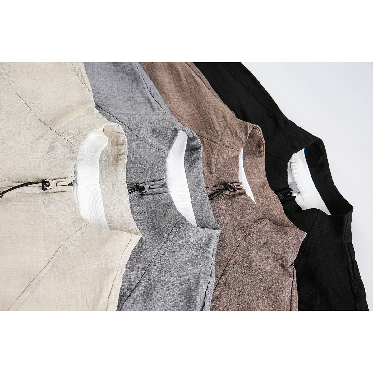 Close-up of four overlapping jackets in cream, gray, taupe, and black, showing their collars and zipper pulls.