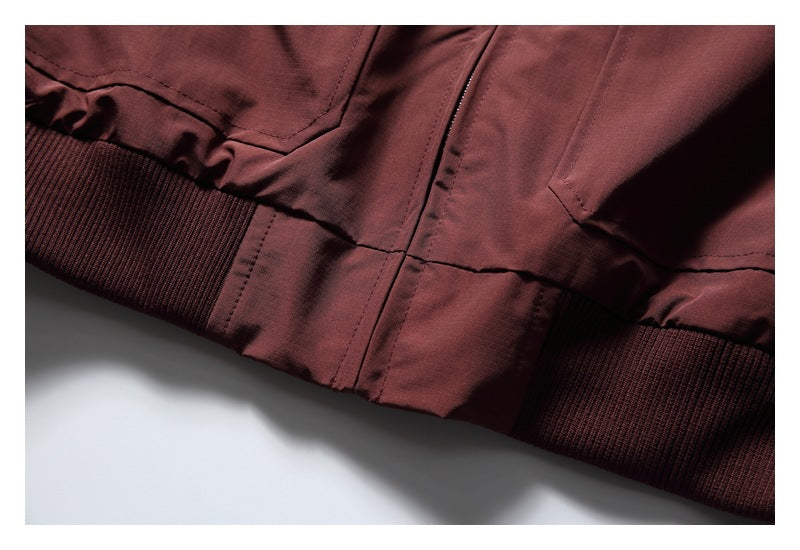 Close-up of the burgundy jacket's front zipper, lower seam, and ribbed hem.